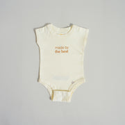 Flat image of cream colored baby onesie with the words "Made by the best" in gold letters